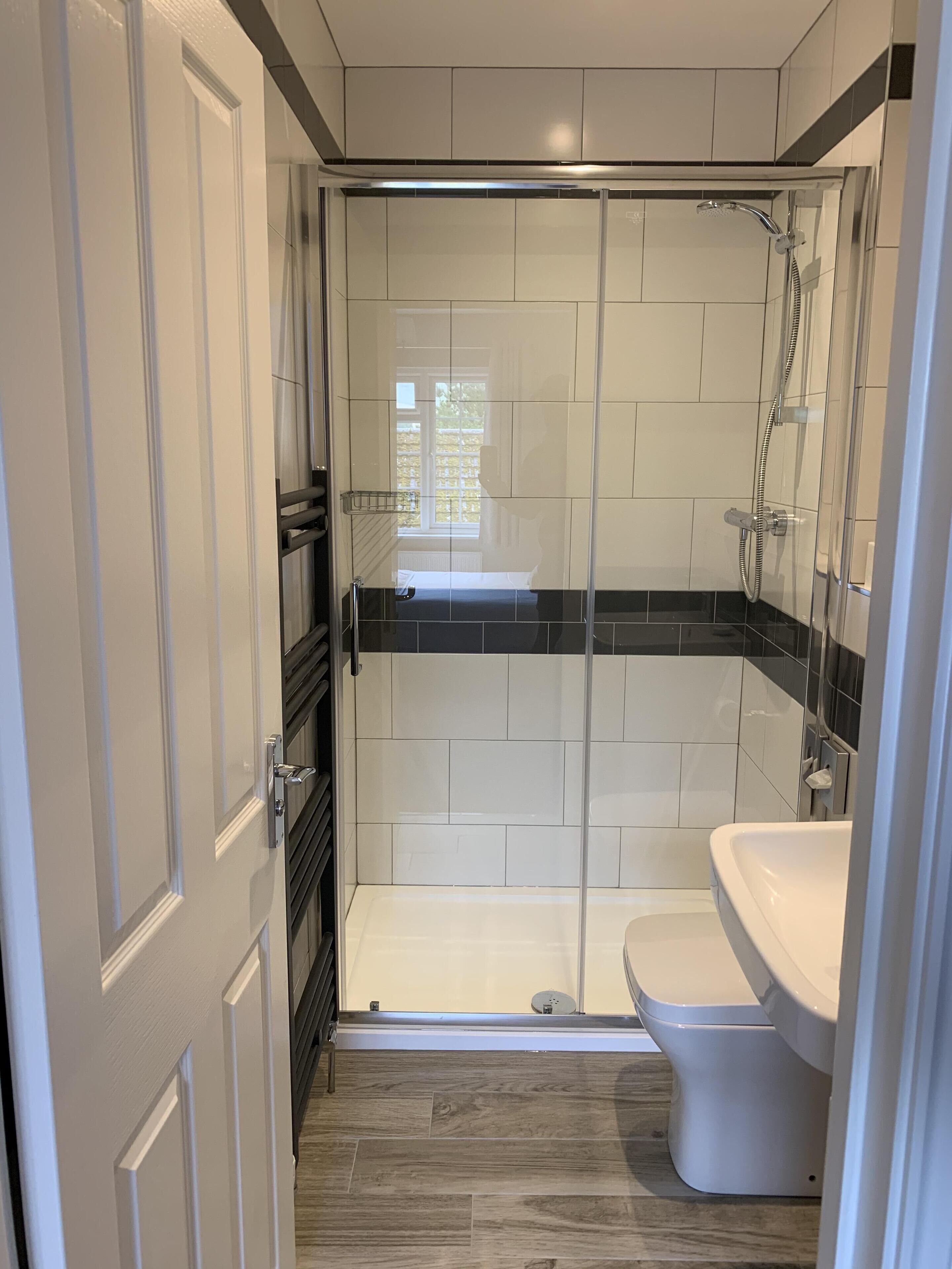 A modern bathroom with a glass-enclosed shower, a white toilet, and a wooden floor.