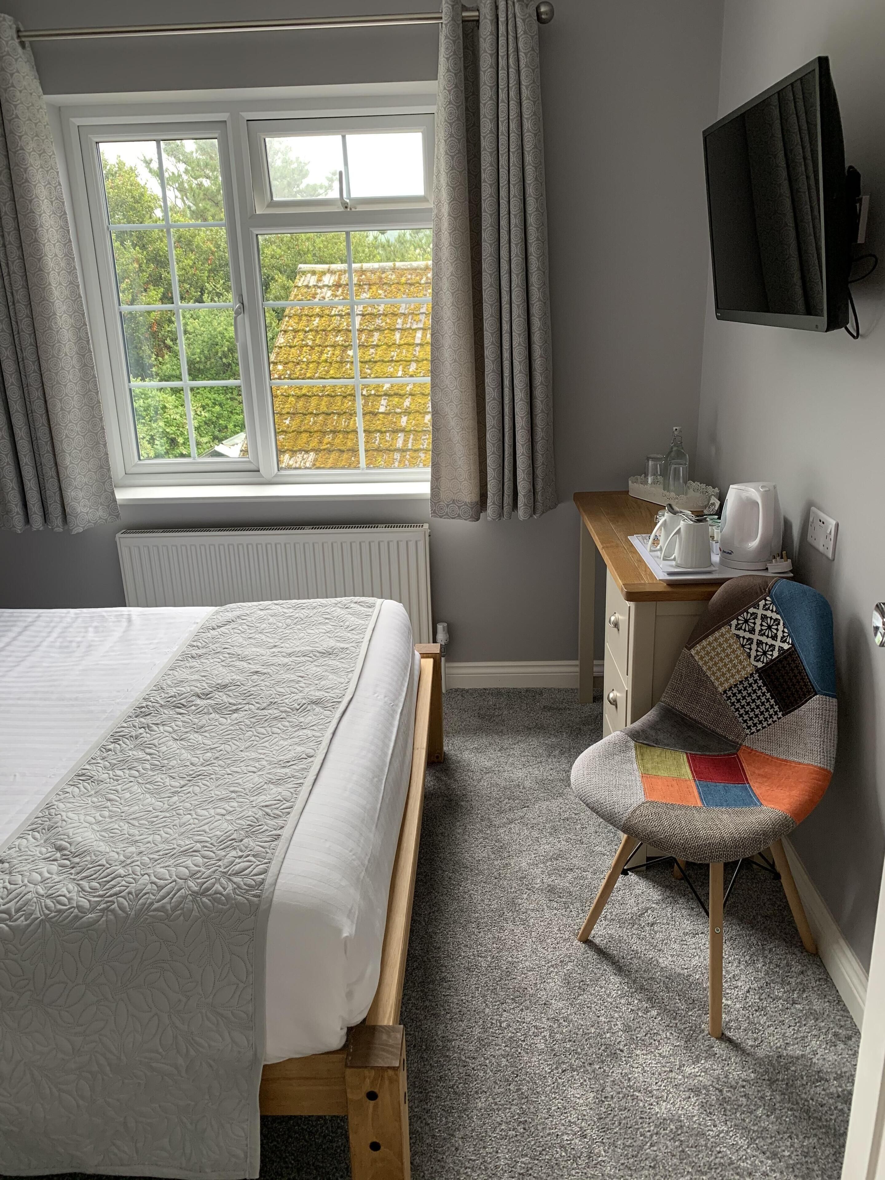 A bedroom with a bed, a desk, a chair, a radiator, a window with curtains, and a television on the wall.