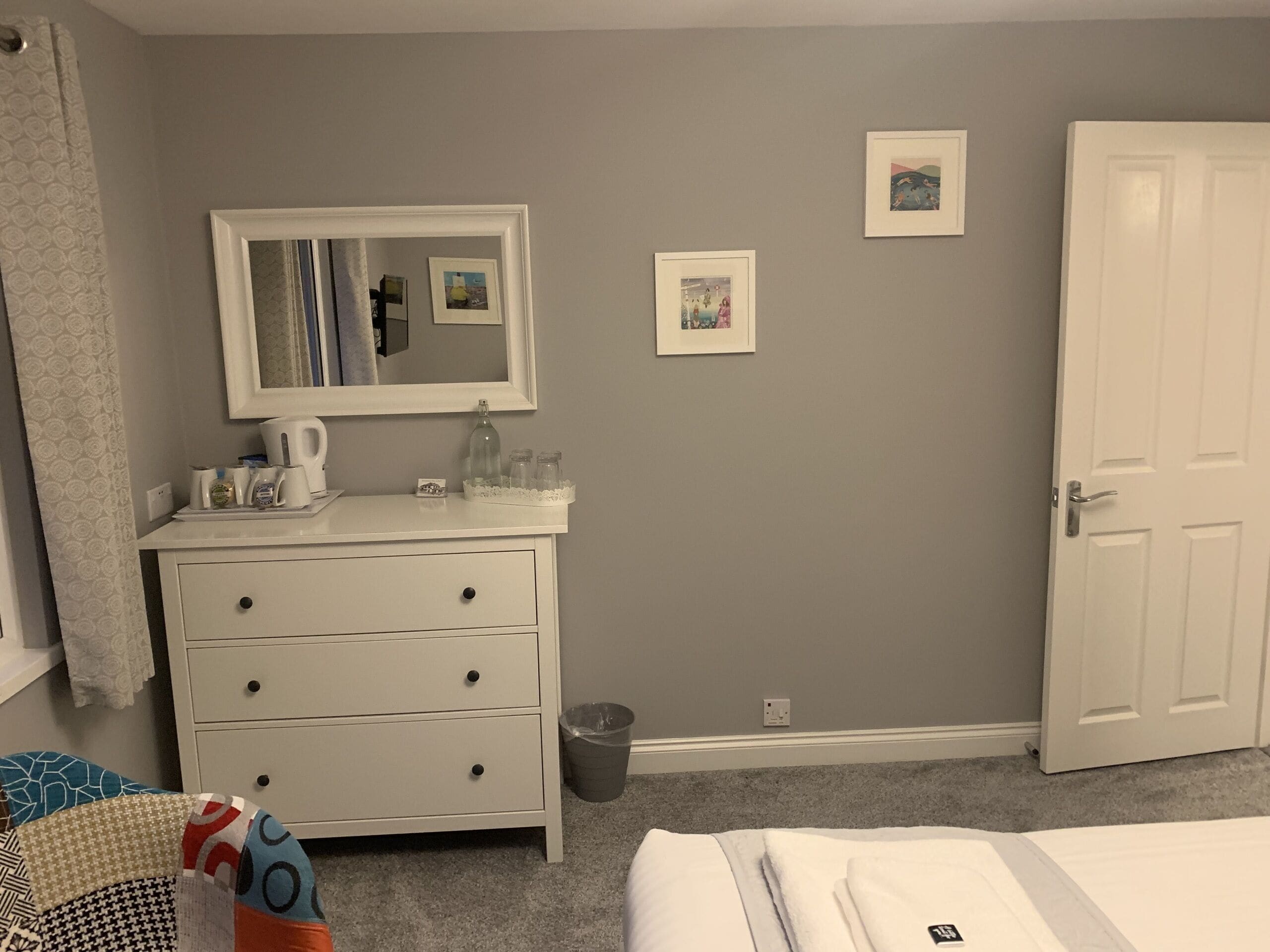 A bedroom with a white dresser, a mirror, and two framed pictures on the wall.