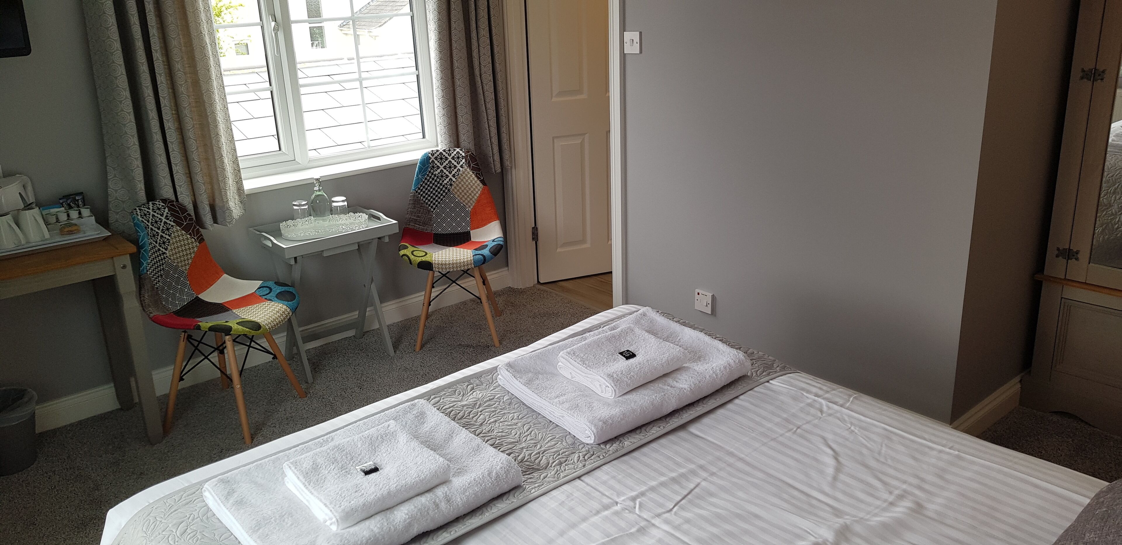 A hotel room with a bed, two chairs, a desk, a window, and a mirror.