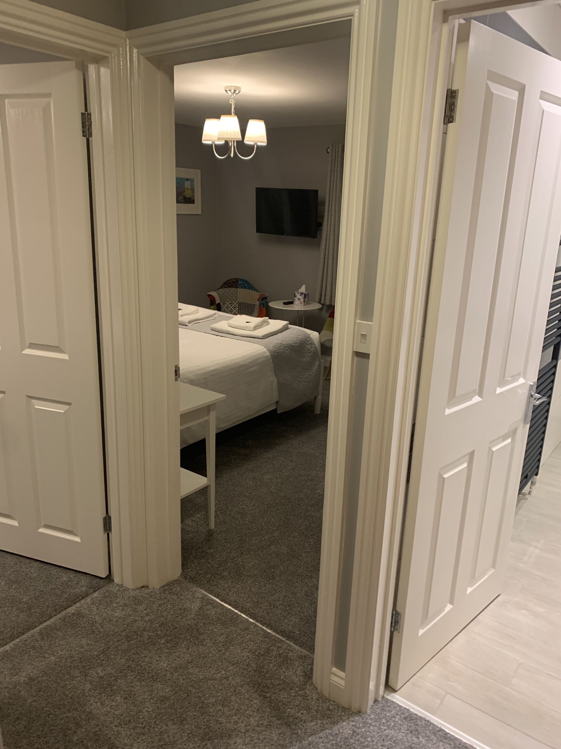 A hotel room with a bed, a bedside table, a chair, a TV, and a chandelier.