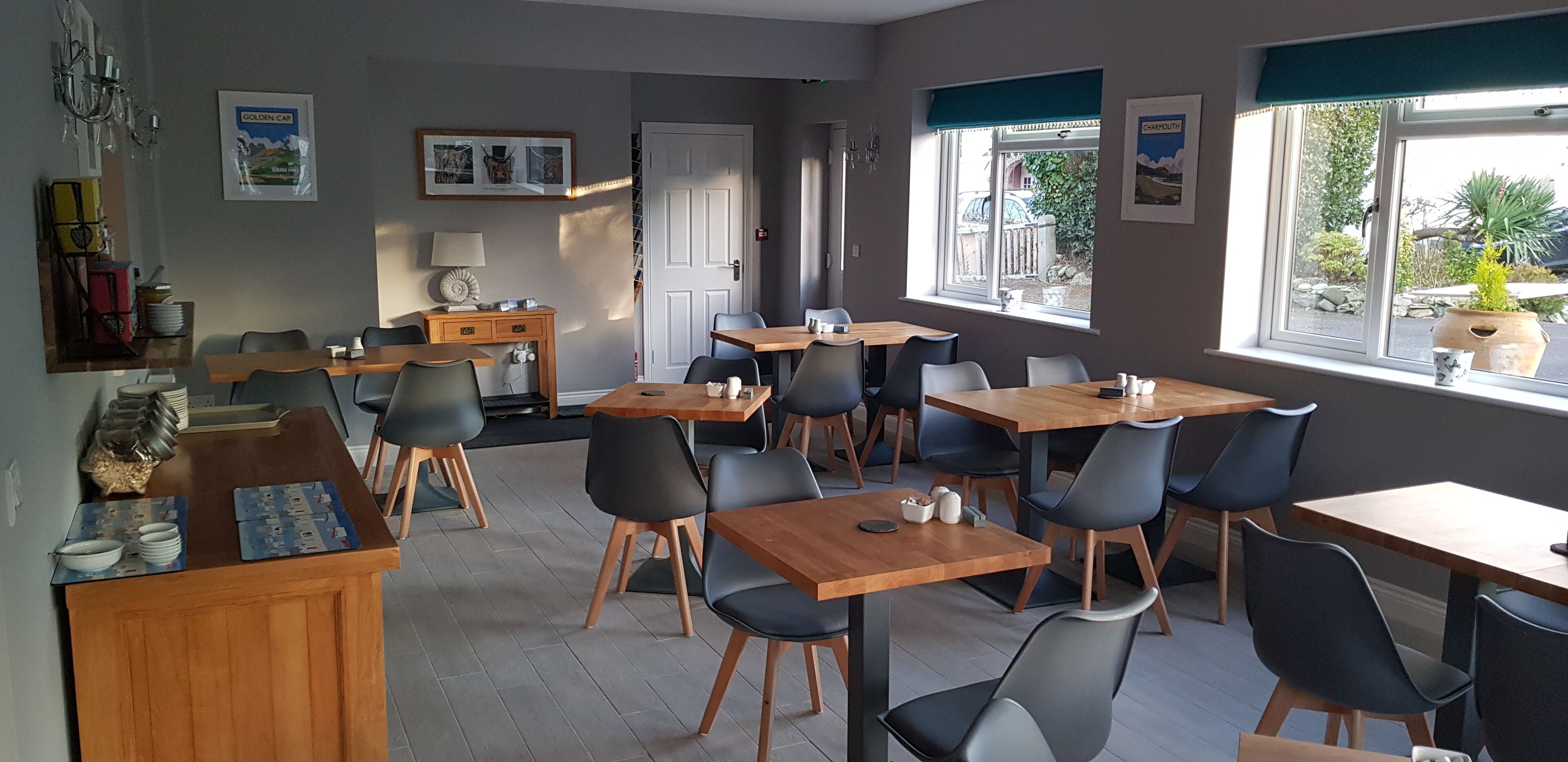 Un comedor con varias mesas y sillas, una barra de madera con una caja registradora y un ventanal con vistas al exterior.
