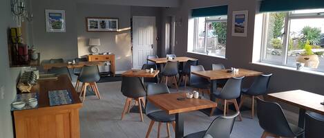Un comedor con varias mesas y sillas, una barra de madera con una caja registradora y un ventanal con vistas al exterior.