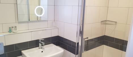 A bathroom with a white sink, a mirror with a light, and a shower area.