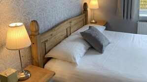 A neatly made bed with white linens, a wooden headboard, and a gray pillow. There is a bedside table with a lamp and a box, and a framed picture on the wall. - Hensleigh House (Bridport)