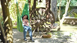 A person relaxing on a hammock in a garden with a large wooden wheel structure in the background. - Pouso Dos Anjos (Lisbon)