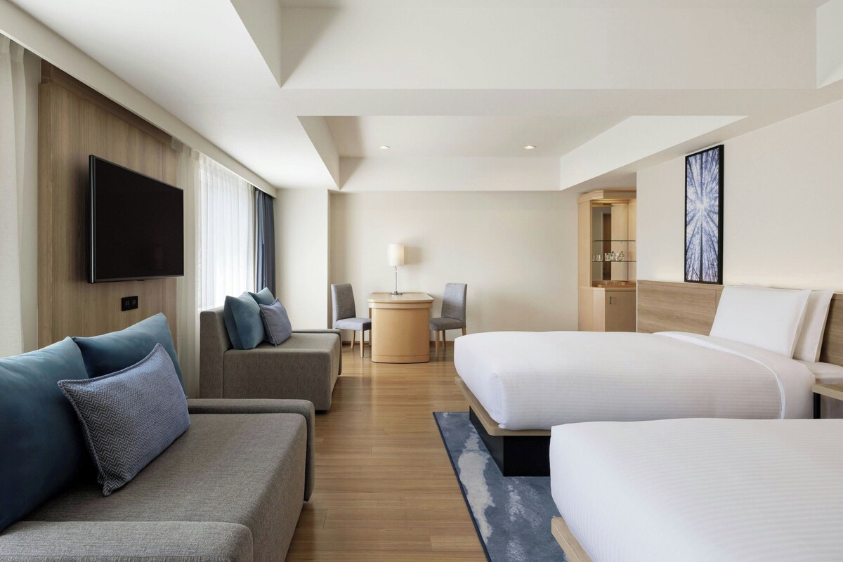 A modern hotel room with a large bed, a sofa, a desk, and a flat-screen TV.