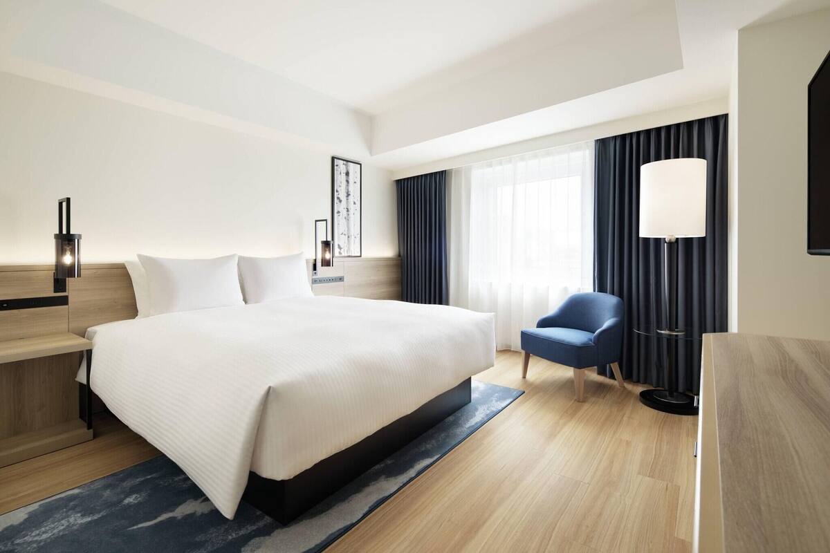 A hotel room with a large bed, a desk, a chair, a lamp, and a window with curtains.