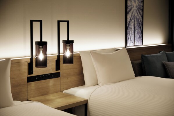 Habitación de hotel con cabecera de madera, dos mesitas de noche, cama con ropa de cama blanca y dos lámparas fijadas a la pared.