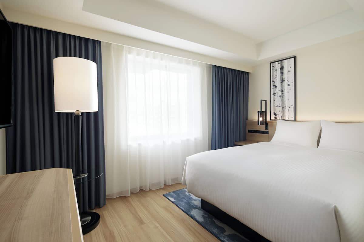 A hotel room with a large bed, a desk, a lamp, and a window with curtains.