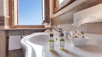 A bathroom with a white sink, two bottles of olive oil, and a box of olive oil shampoo.