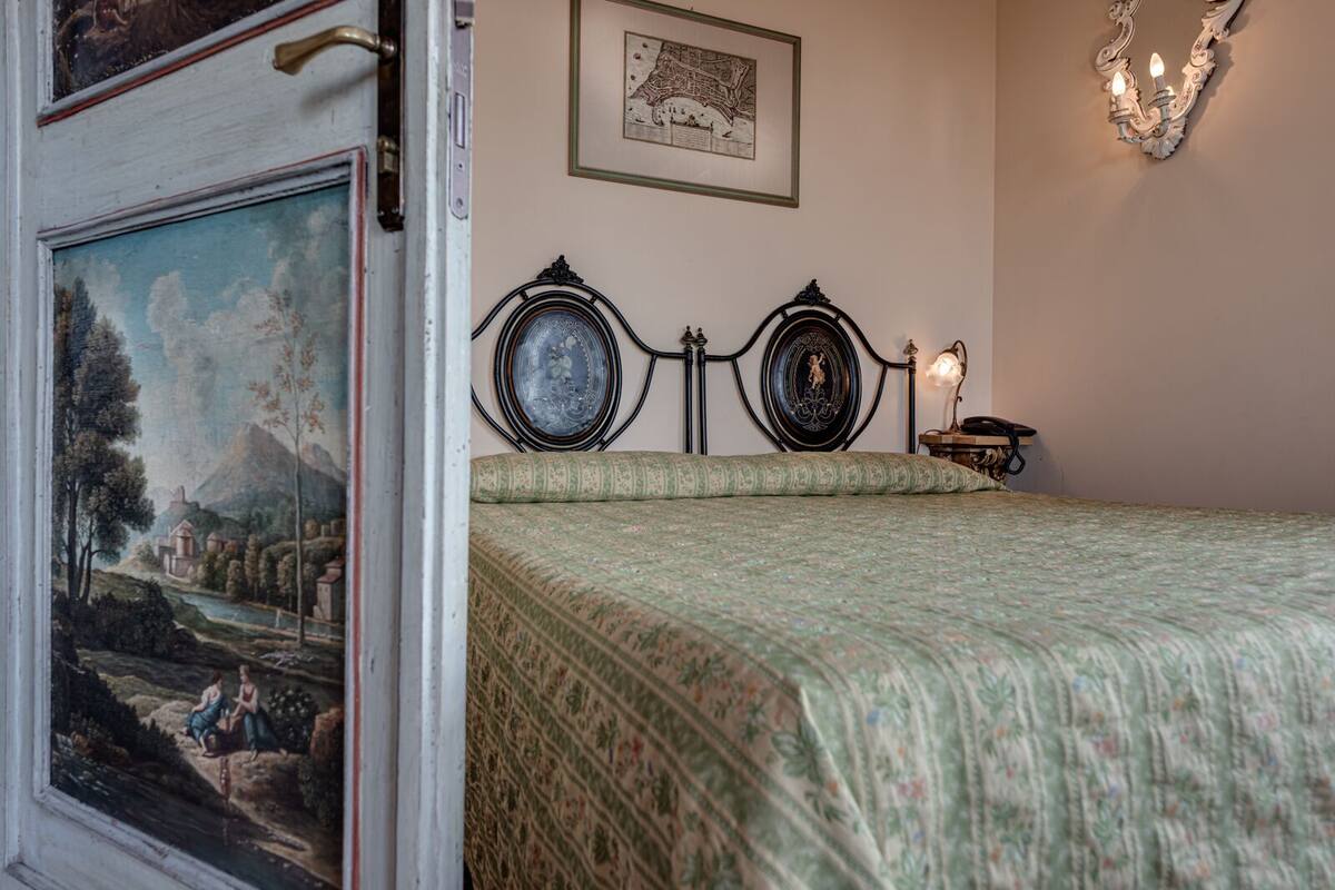 Une chambre à coucher avec un lit, un tableau accroché au mur, une carte et un chandelier.