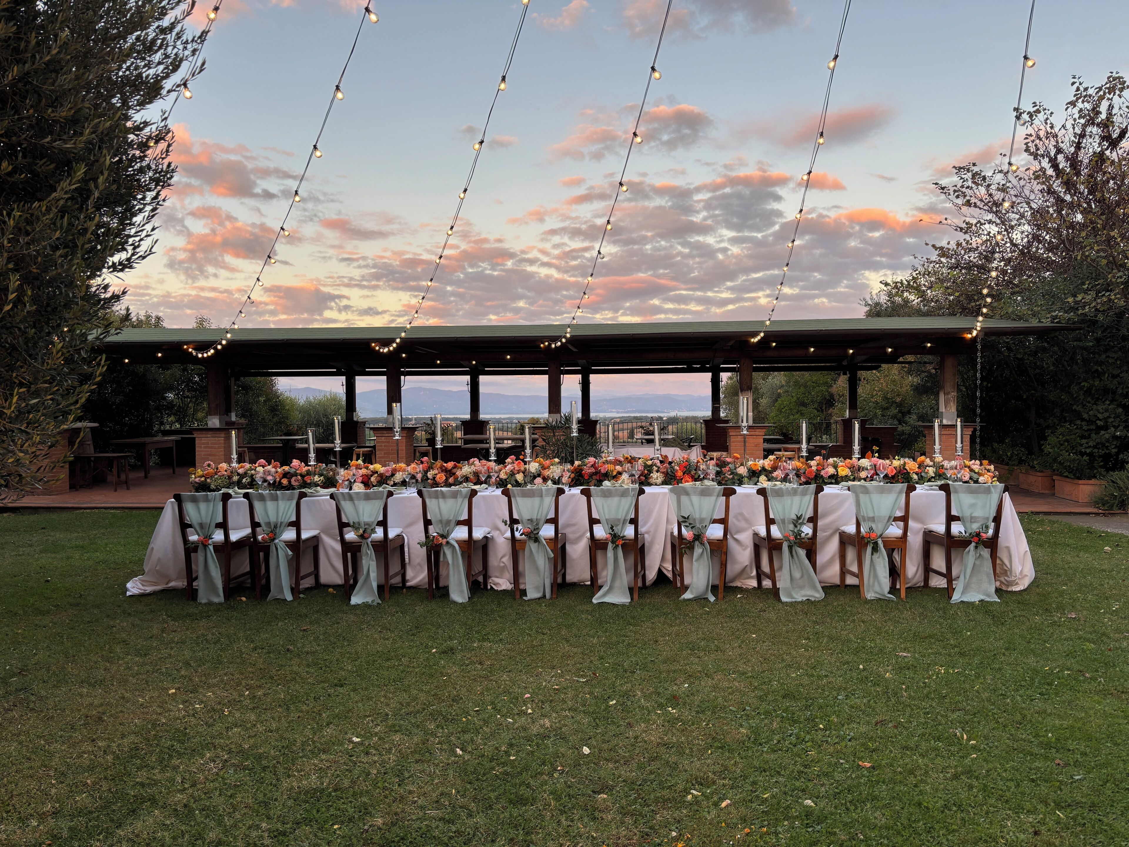 An outdoor dining area with tables set for a meal, surrounded by greenery and a scenic view.