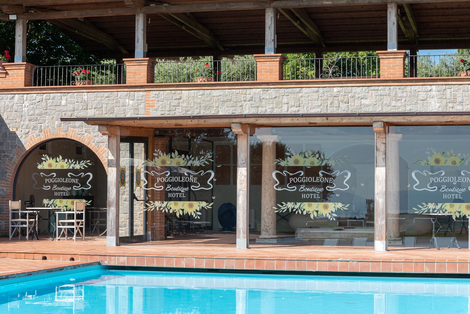 Un hotel con fachada de piedra, ventanas grandes con girasoles y una zona de piscina.