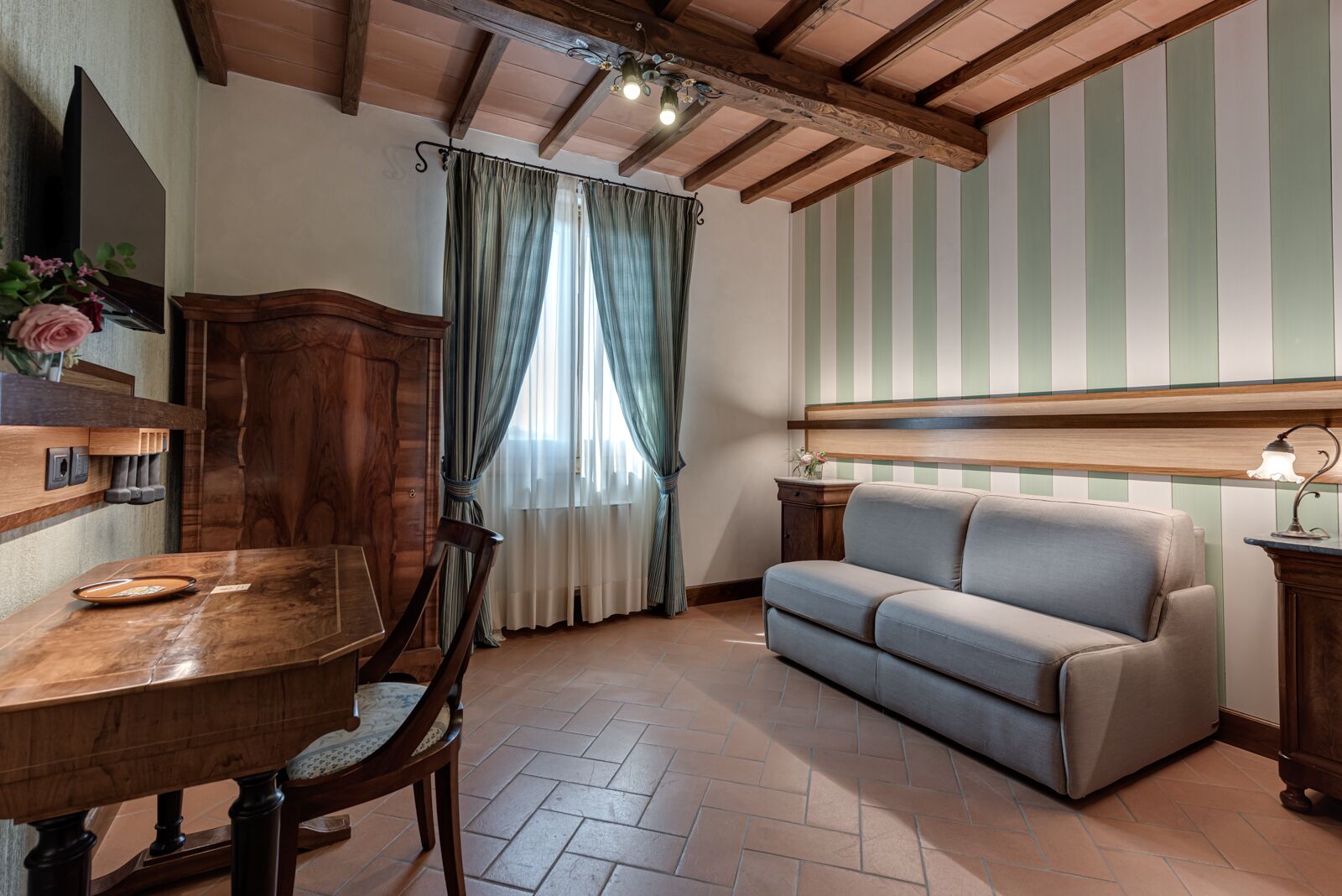 A room with a wooden dining table, chairs, a sofa, a wooden cabinet, and a window with curtains.