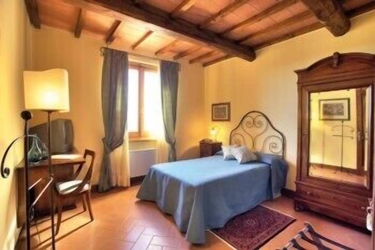 Une chambre à coucher comprenant un lit, une chaise, un bureau avec une lampe, une commode et une fenêtre avec des rideaux.