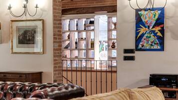 A room with a leather sofa, a wooden cabinet, a framed picture, a wine rack, and a colorful abstract painting.