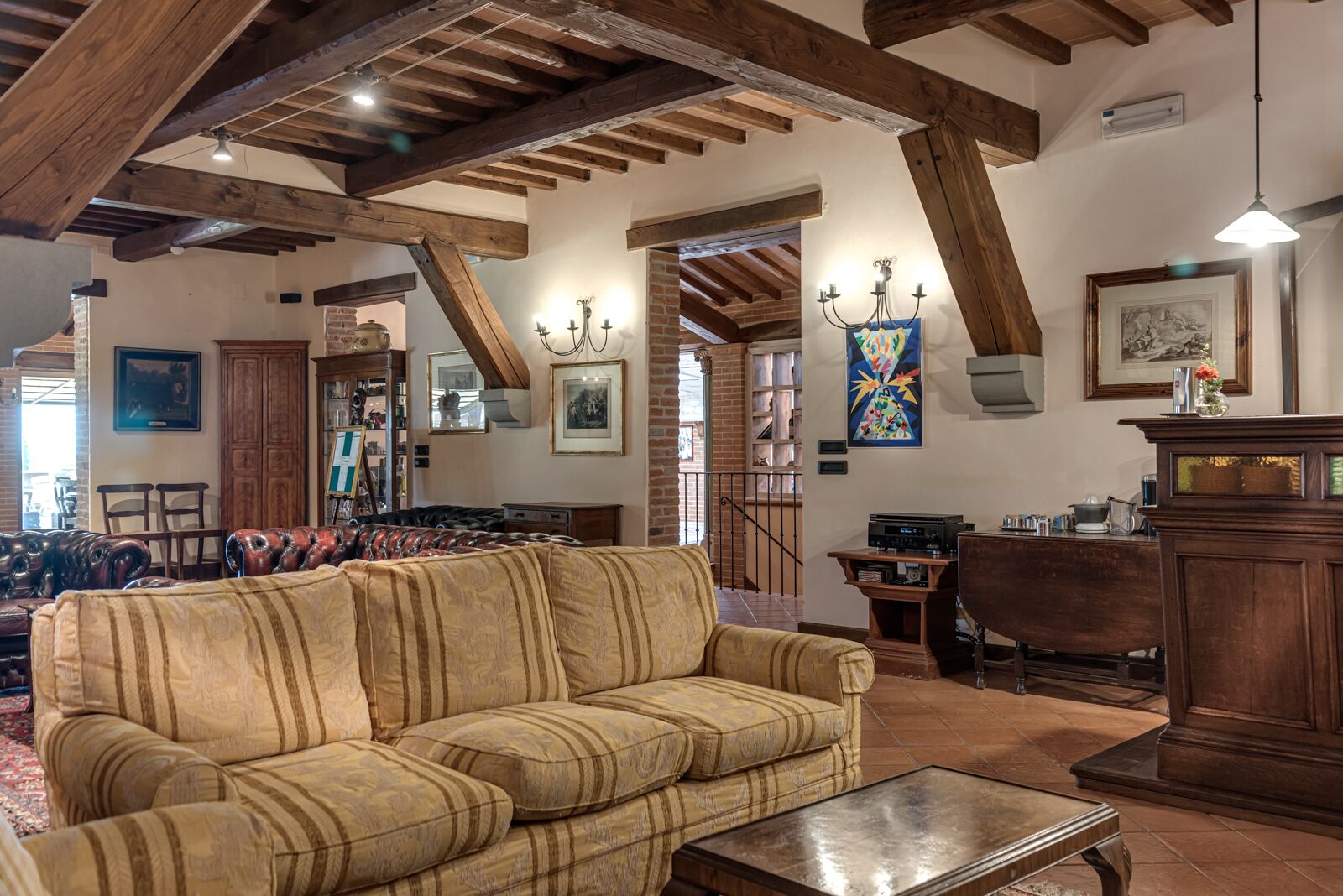 Un salón amplio con un sofá grande, vigas de madera, chimenea y comedor con mesa y sillas de madera.