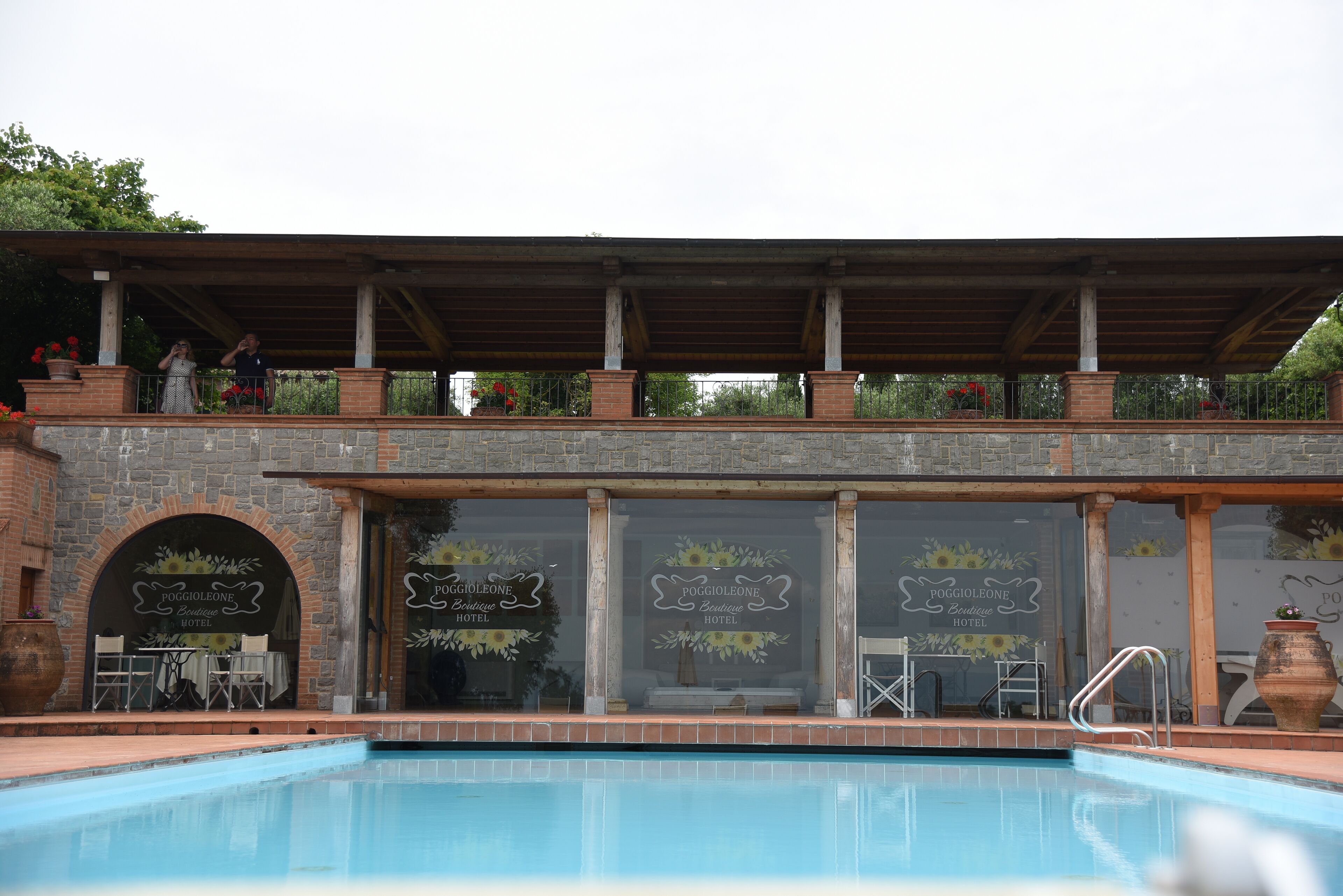 Un'area piscina con portico coperto, pareti in pietra e un cartello per l'Hotel Boutique Poggioleone.