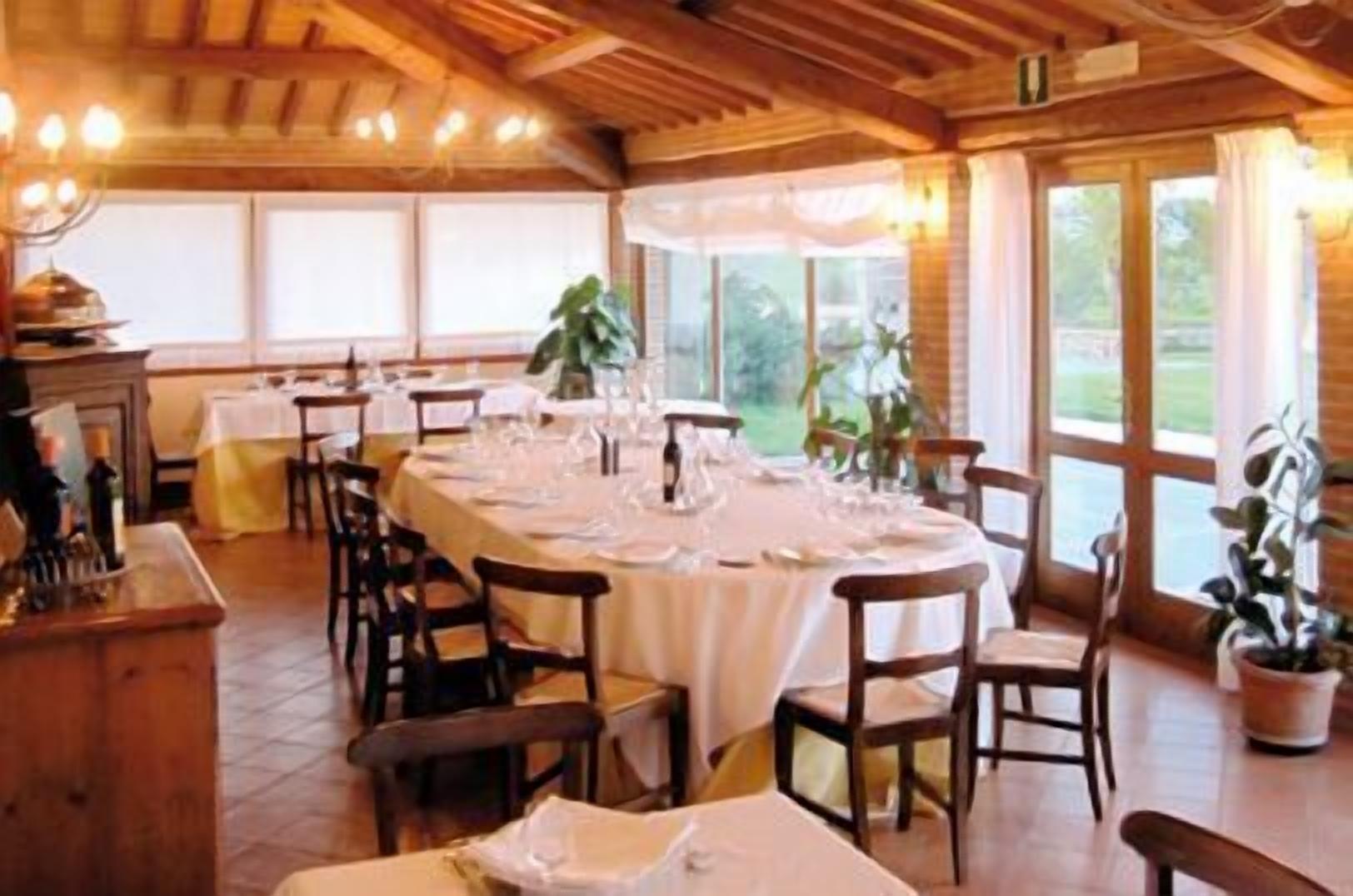 Un comedor con una larga mesa dispuesta para una comida, sillas de madera y ventanas amplias con cortinas.
