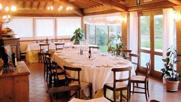 Un comedor con una larga mesa dispuesta para una comida, sillas de madera y ventanas amplias con cortinas.
