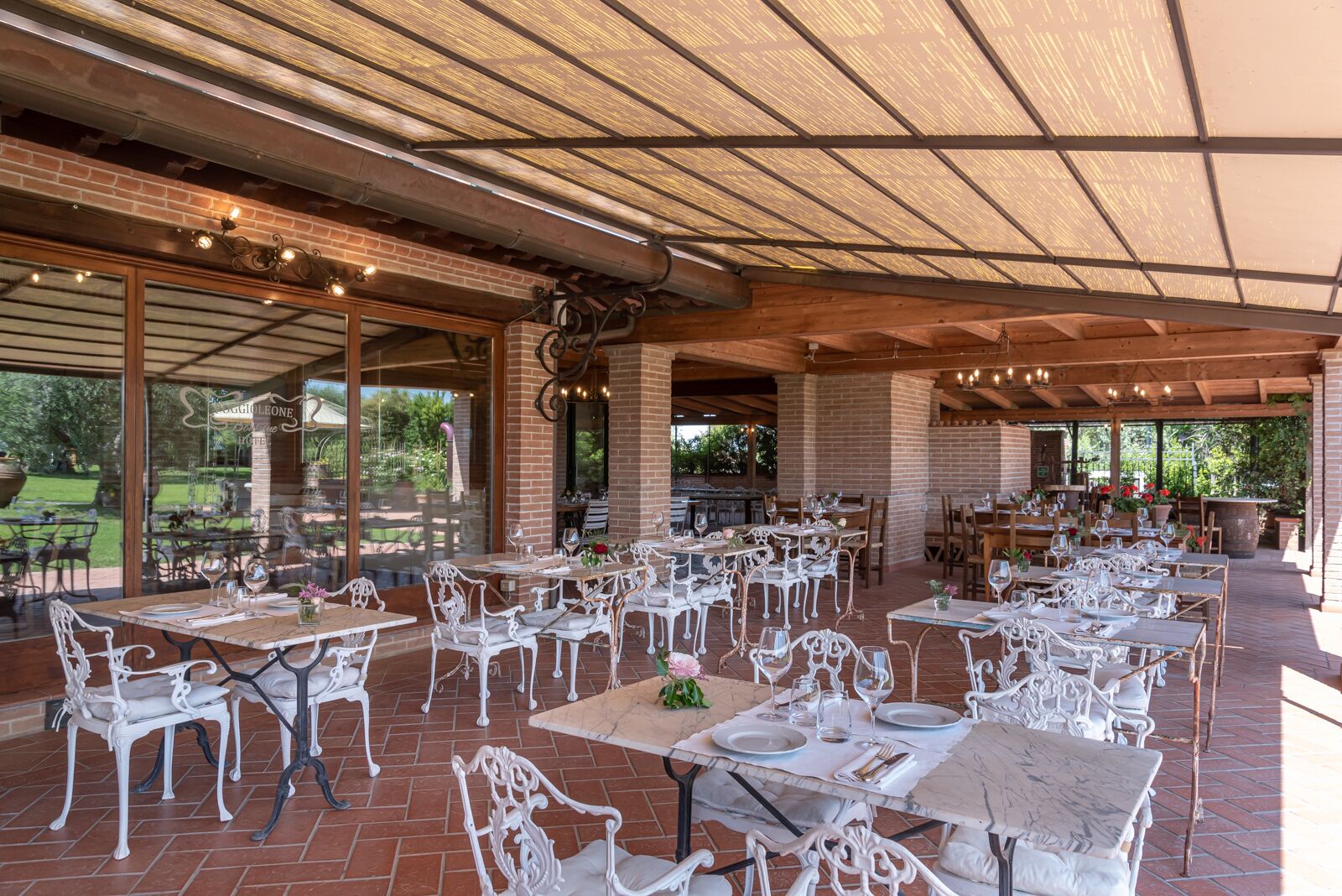 An outdoor dining area with brick walls, white metal chairs, and tables set for dining.