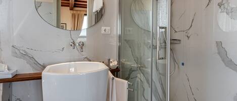A bathroom with a large white sink, a glass shower enclosure, and a marble wall.