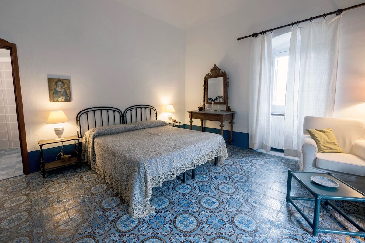 A bedroom with a bed, two bedside tables with lamps, a dresser, a chair, and a window with curtains.