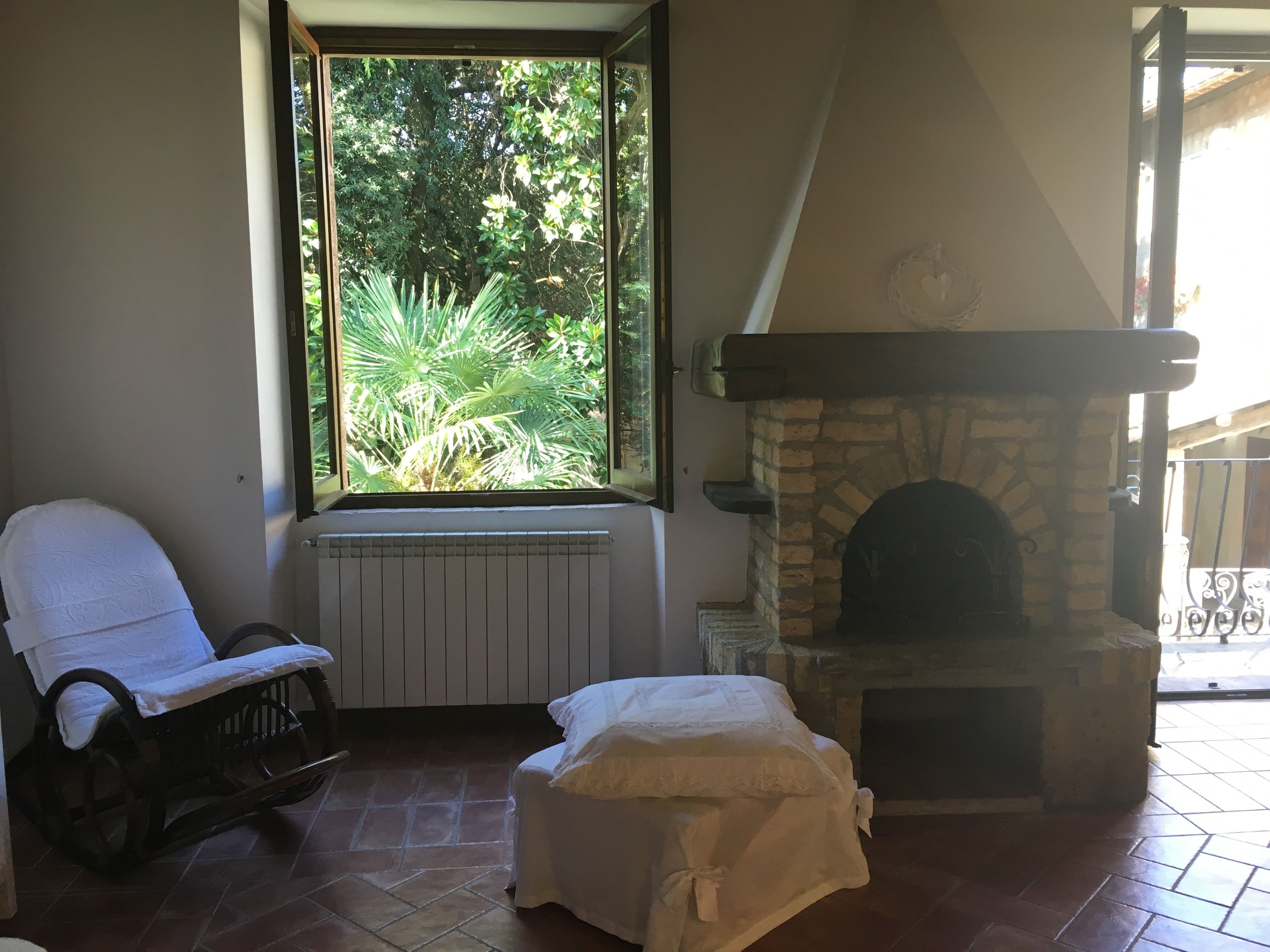 A room with a stone fireplace, a window with a view of greenery, a wheelchair, and a covered bench.