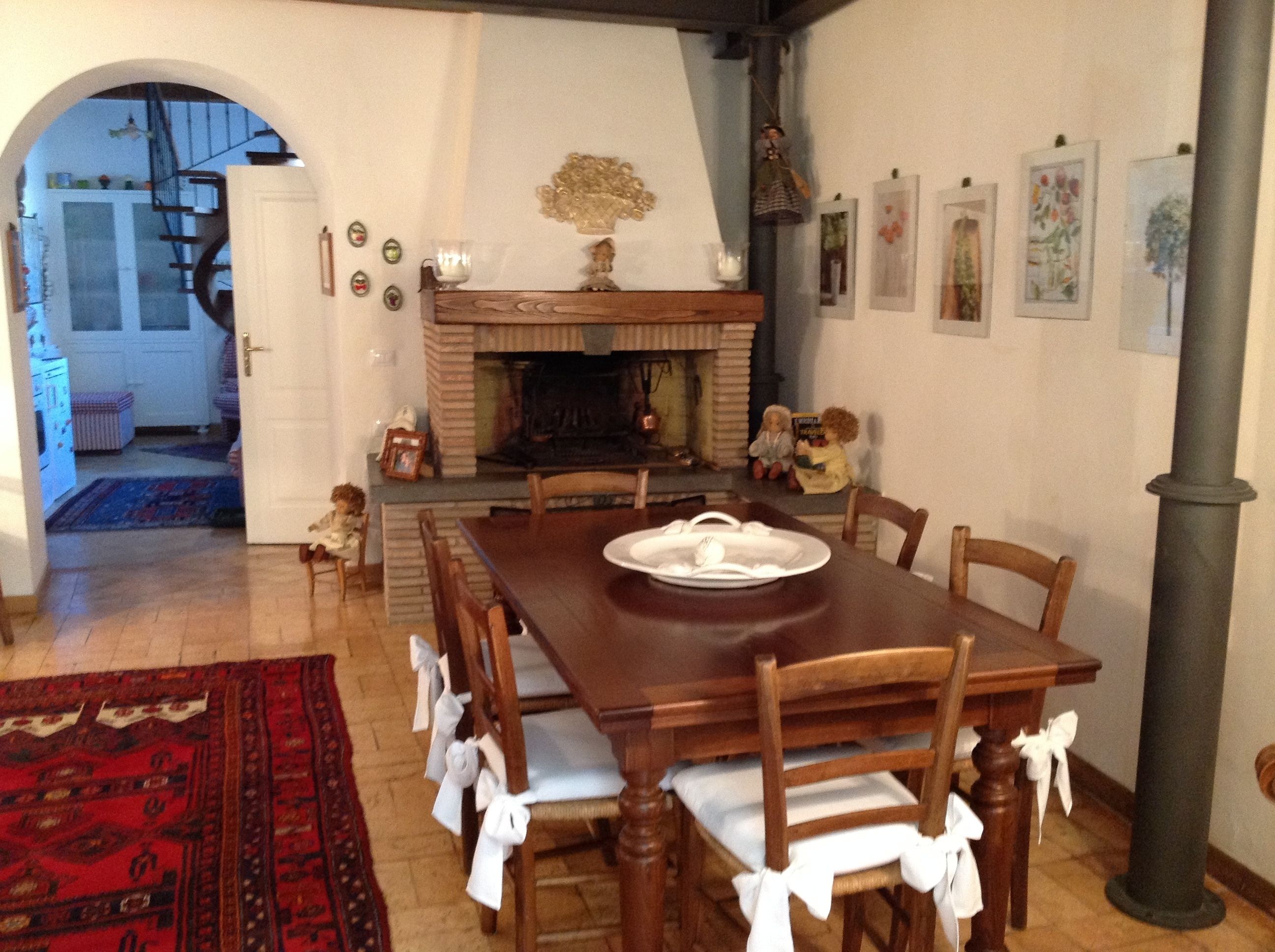 A dining area with a wooden table, chairs, and a fireplace. There is a rug on the floor and a door leading to another room.