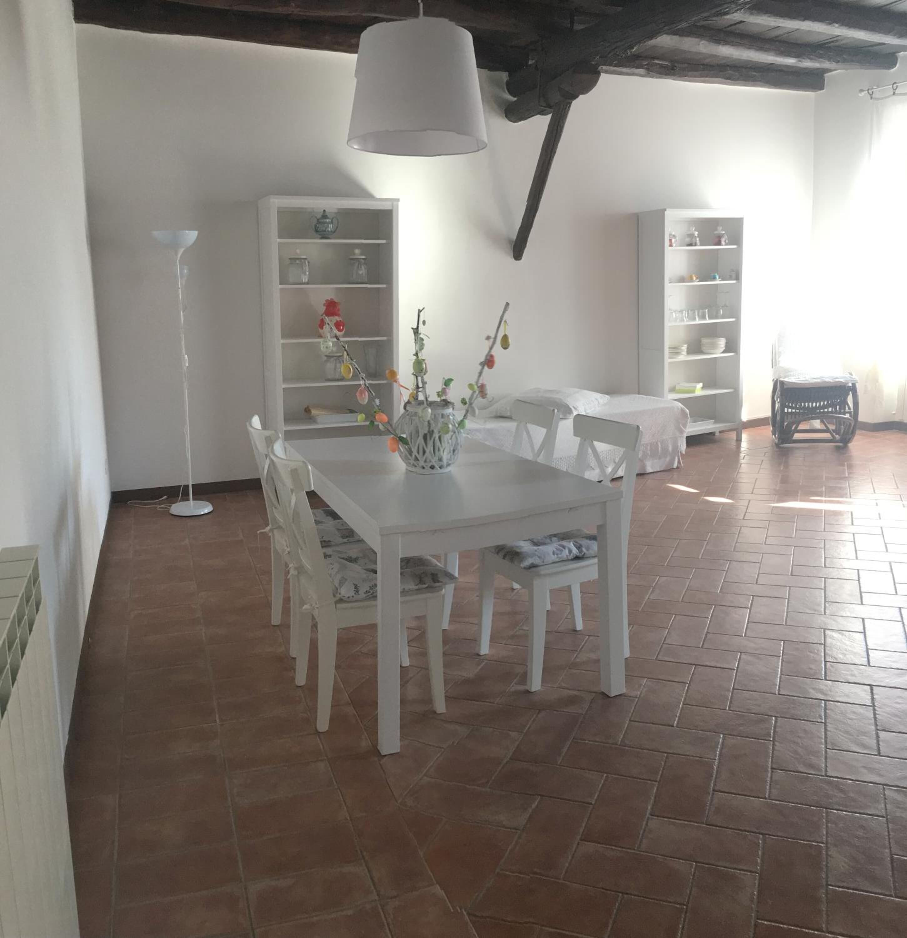A dining area with a white table and chairs, a hanging light fixture, and a tiled floor.