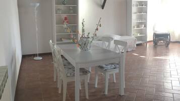 A dining area with a white table and chairs, a hanging light fixture, and a tiled floor.