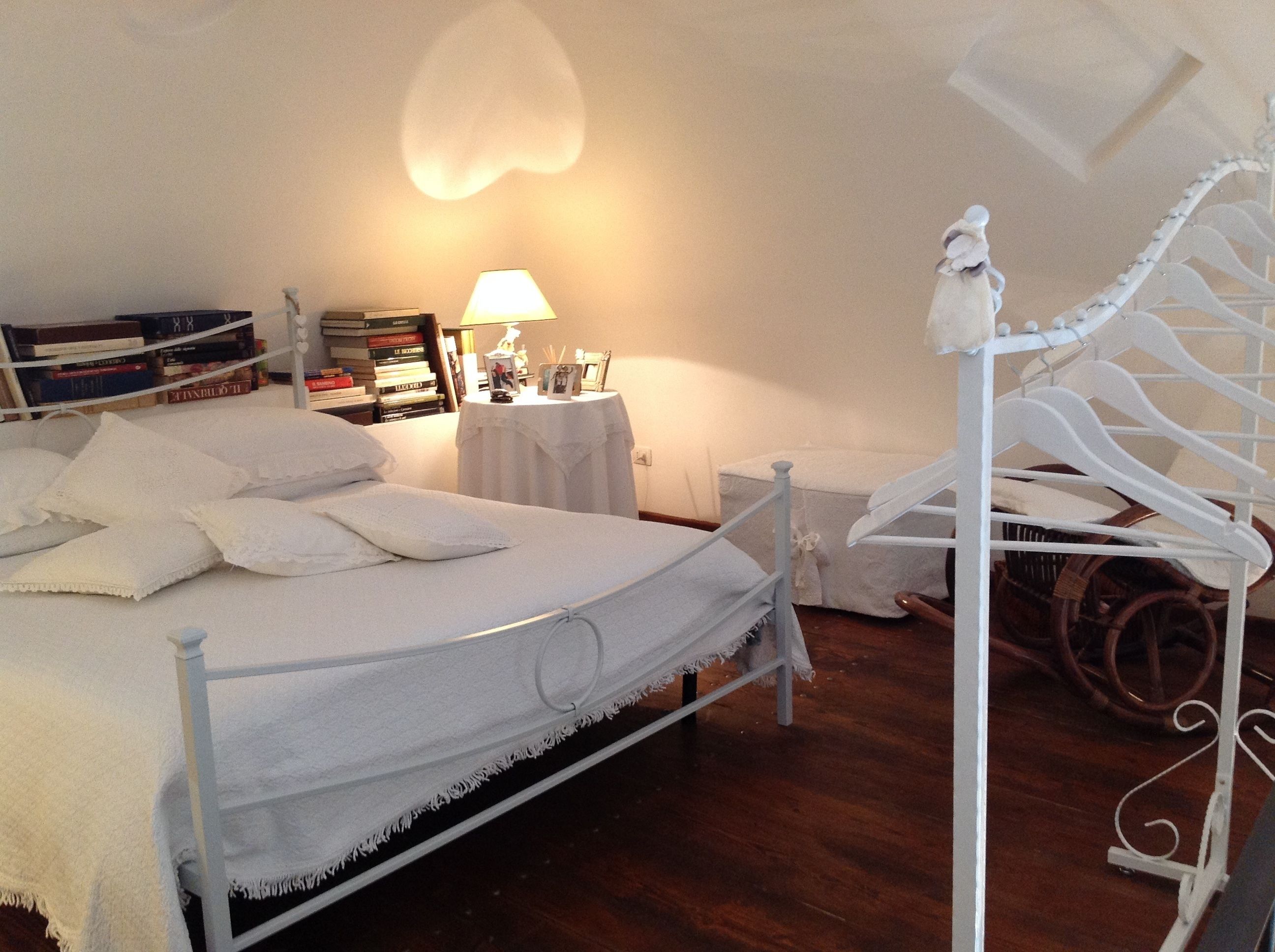 Un dormitorio con una cama, una mesita de noche con lámpara, una estantería y una escalera en espiral blanca.