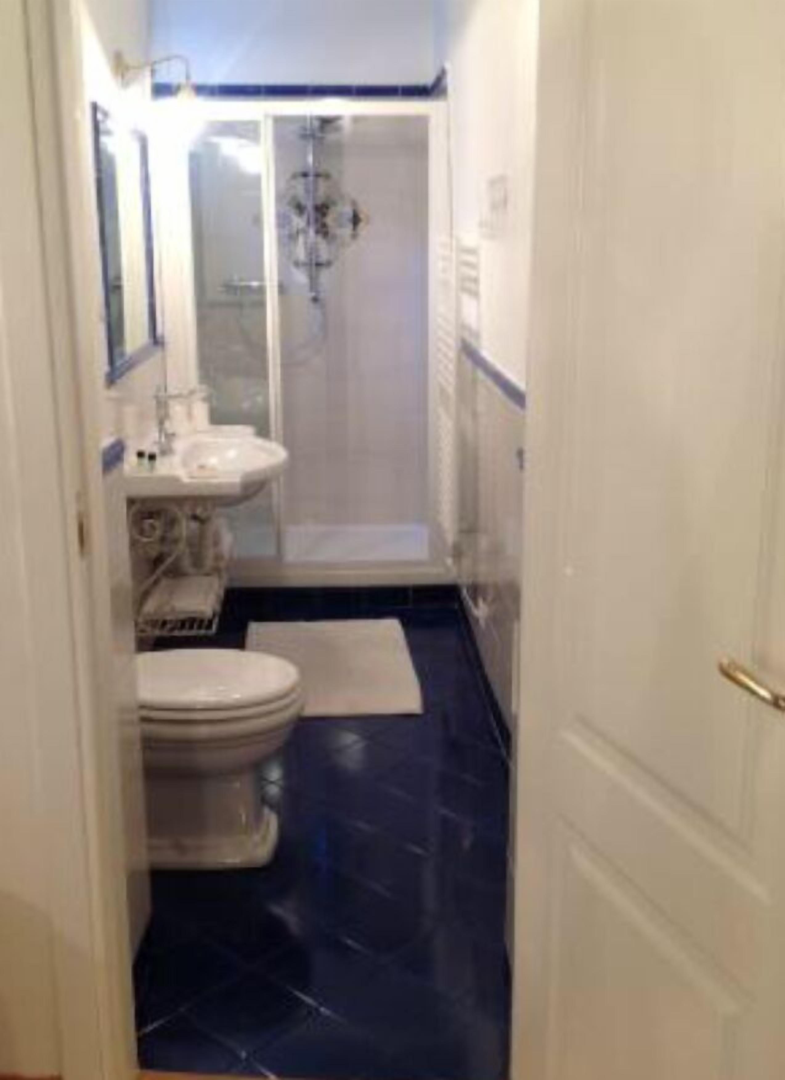 A narrow bathroom with a toilet, sink, and shower area.
