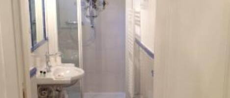 A narrow bathroom with a toilet, sink, and shower area.