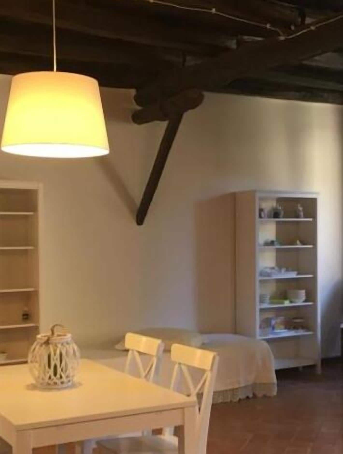 Ein Essbereich mit einem weißen Tisch und Stühlen, einer Hängelampe und einer weißen Schranke mit Regalen.