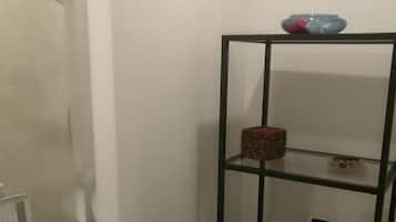 A bathroom with a glass shower enclosure, a black metal shelf unit with a red basket, and a hairdryer on the lowest shelf.