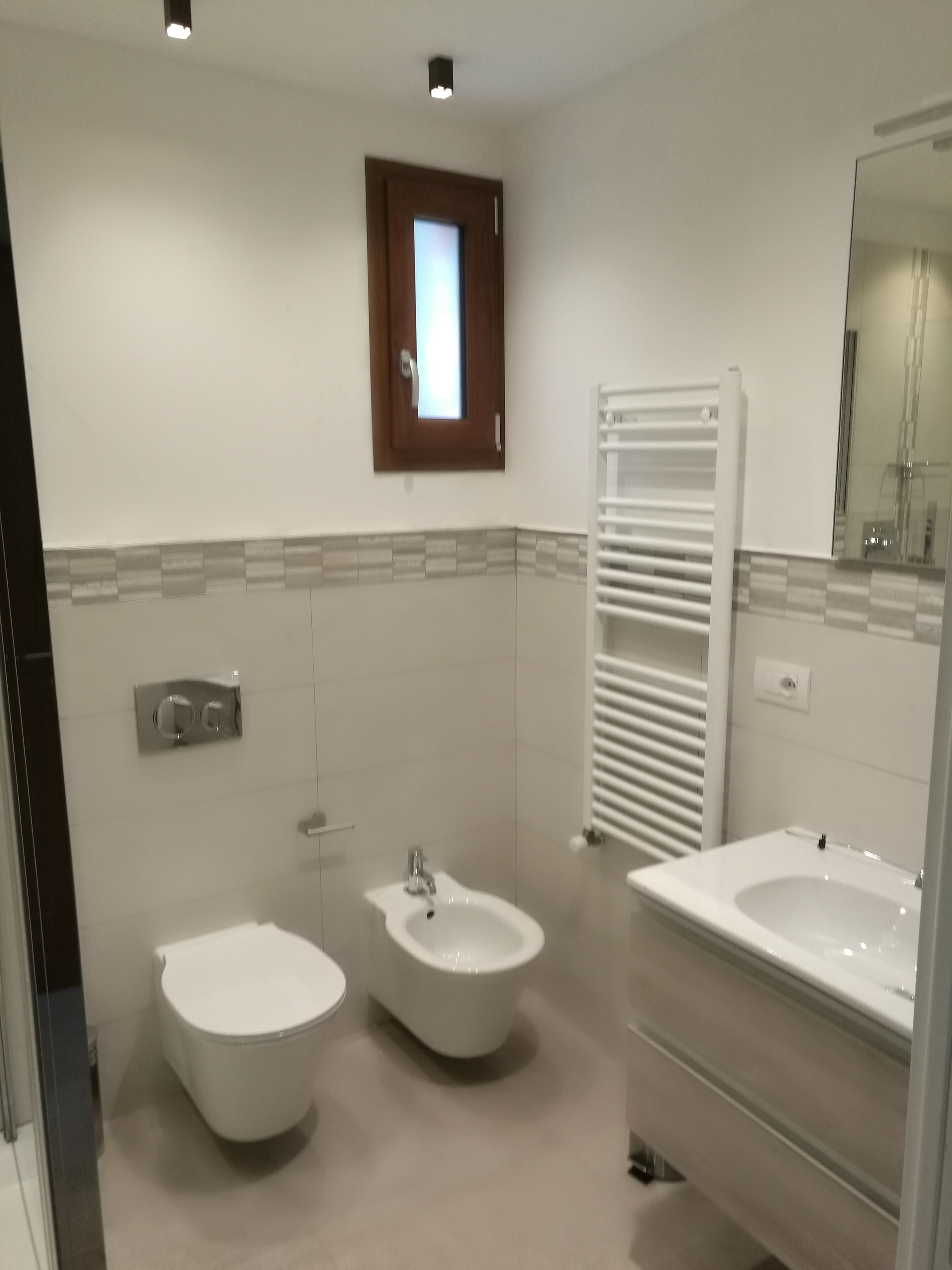 Un baño moderno con dos bidés, un lavamanos, un espejo y un perchero para toallas.