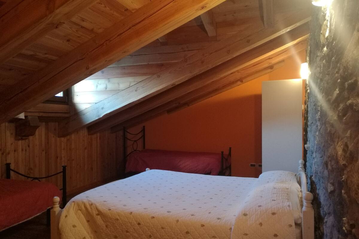 A cozy attic bedroom with wooden beams, a bed with a quilt, and a red chair.