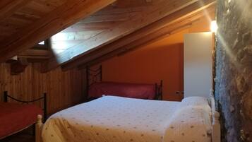 Una camera da letto mansardata accogliente, con travi in legno, un letto con copriletto e una poltrona rossa.
