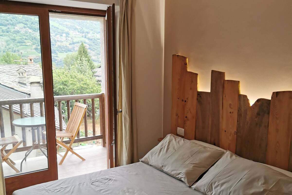 A bedroom with a wooden headboard, a bed with white linens, and a balcony with a table and chairs.