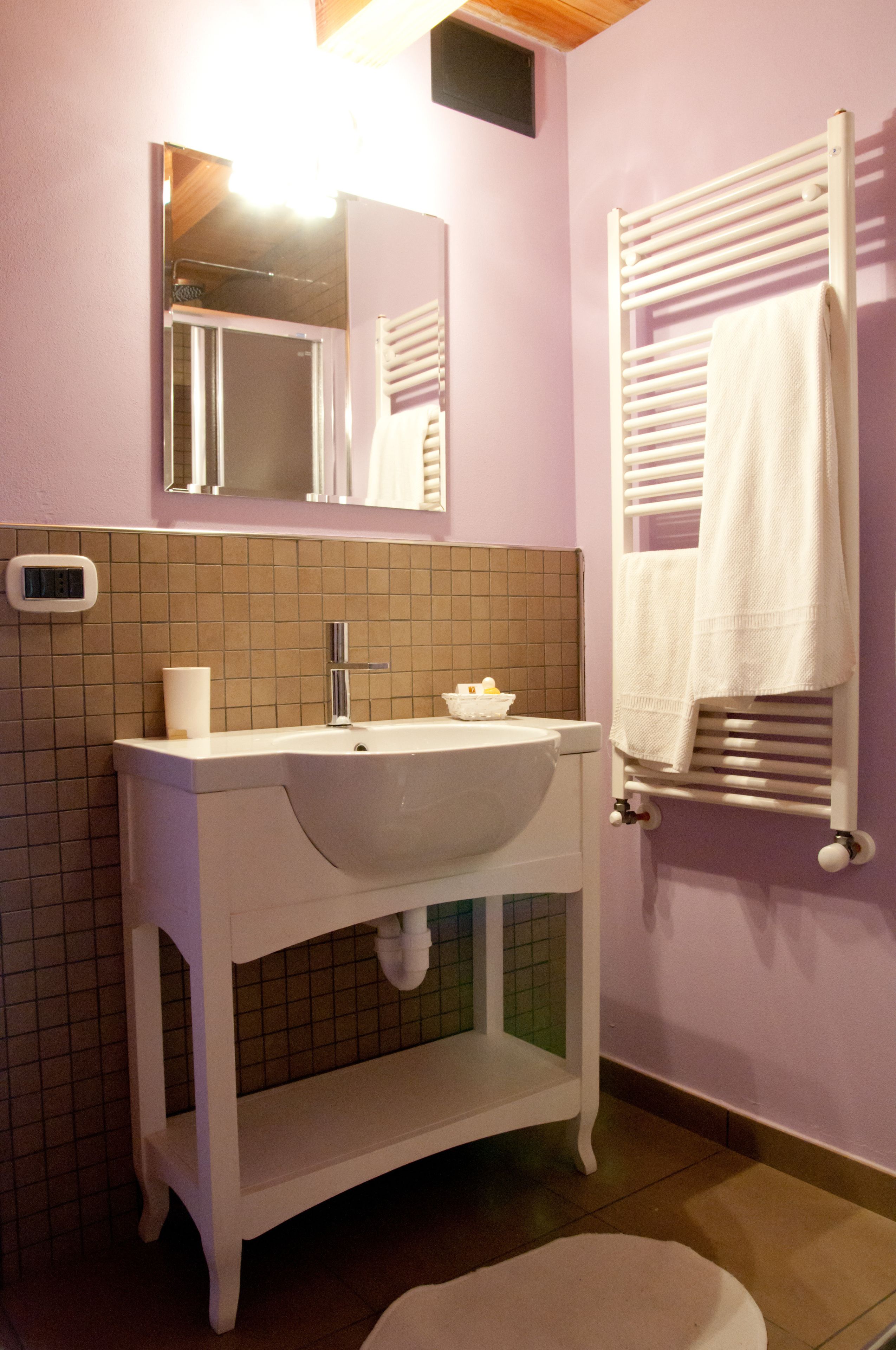 Un baño con lavamanos blanco, espejo y toallero.