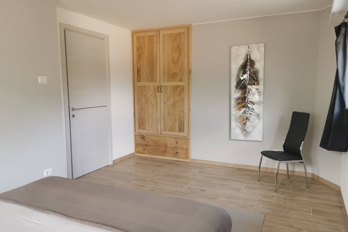 A bedroom with a bed, a wardrobe, a chair, and a painting on the wall.