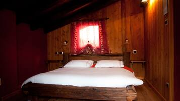 A wooden four-poster bed with white linens, a red curtain, and two wall-mounted lamps.