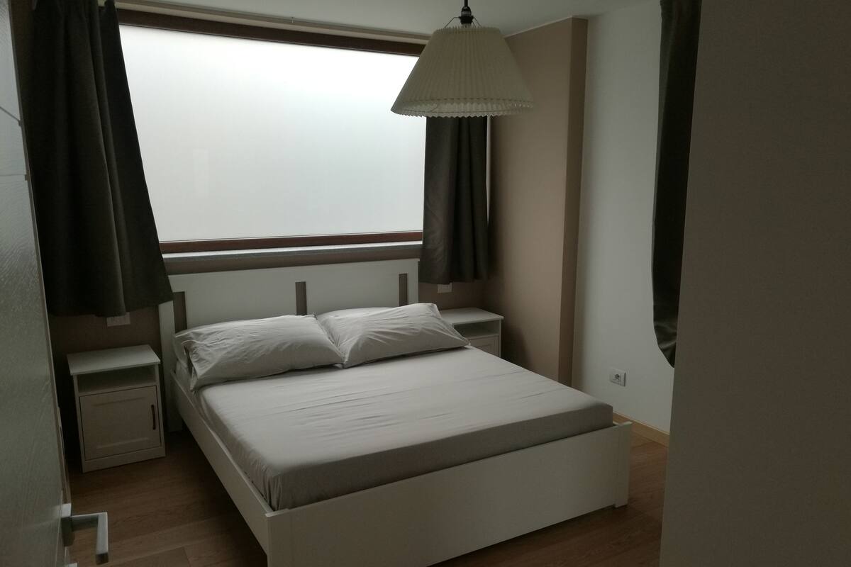 A bedroom with a single bed, nightstands, a window with curtains, and a hanging light fixture.