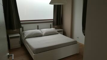 Ein Schlafzimmer mit einem Einzelbett, Nachttischen, einem Fenster mit Vorhängen und einer Hängeleuchte.