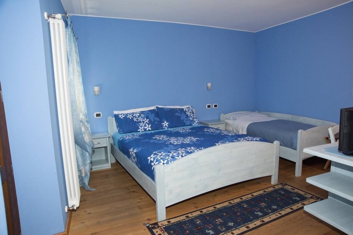 A bedroom with a single bed, a smaller bed, a TV, and a radiator.