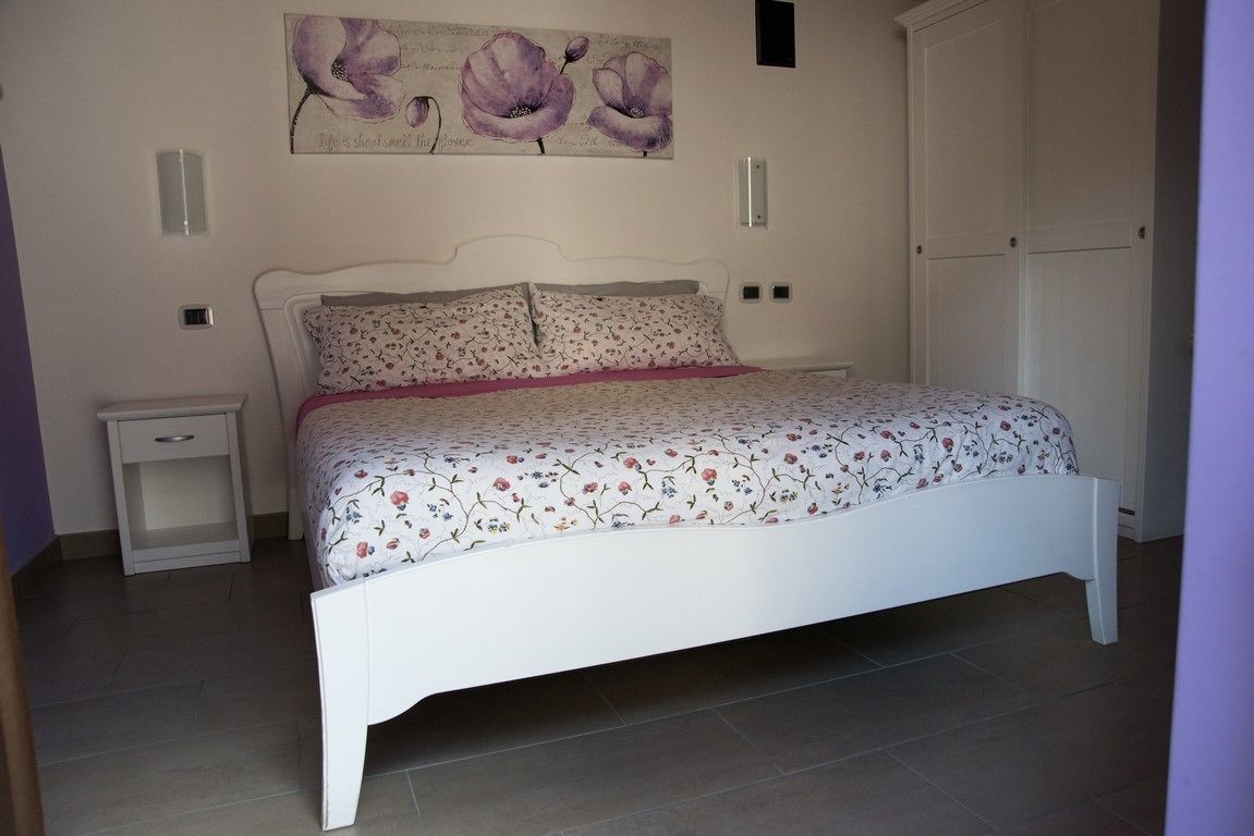 Un dormitorio con una cama blanca, ropa de cama floral, una mesita de noche y una obra de arte colgada en la pared.