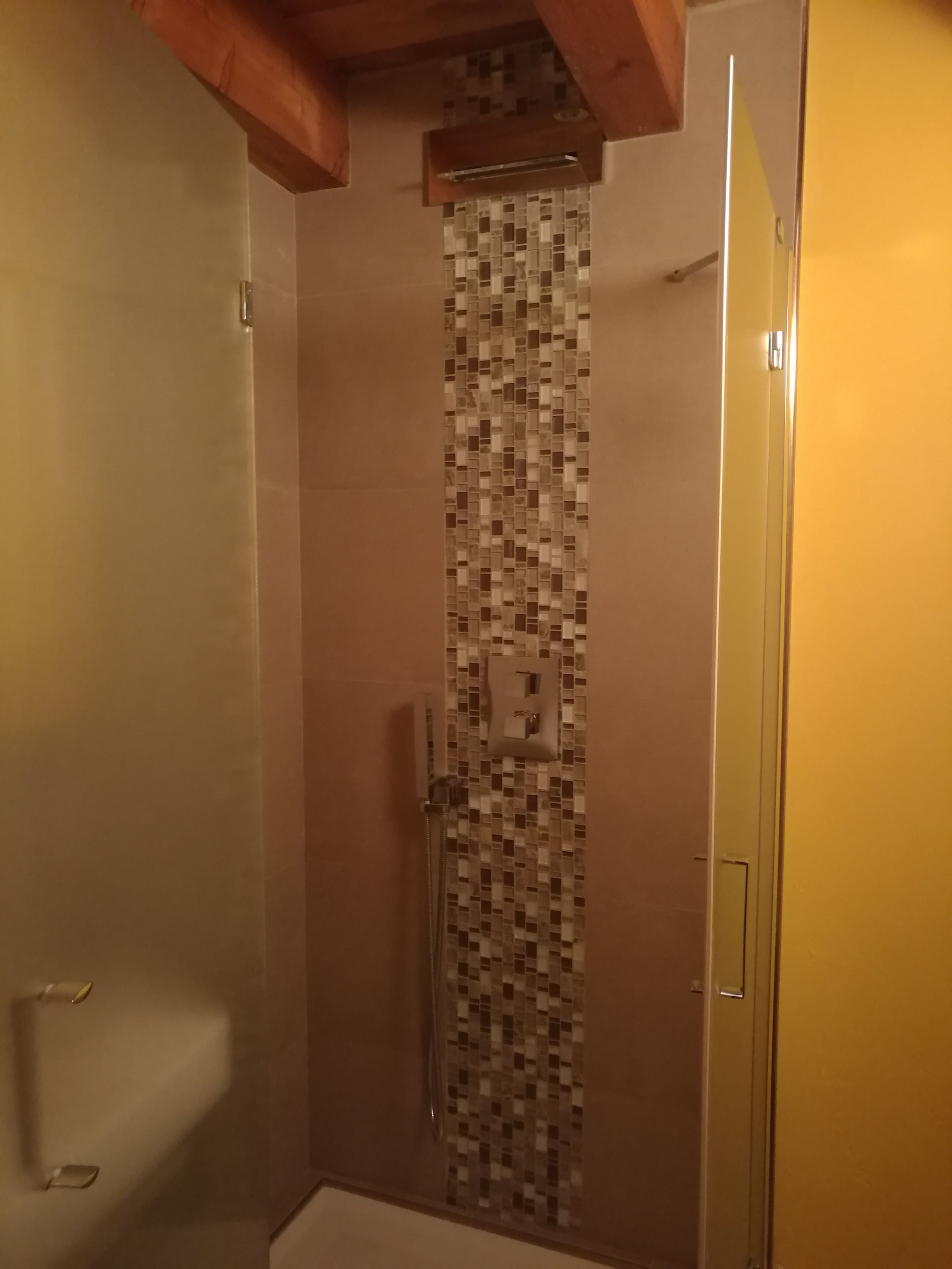 A shower with a tiled wall and a wooden ceiling beam.