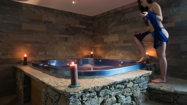 Habitación con paredes de piedra, bañera de hidromasaje y velas.